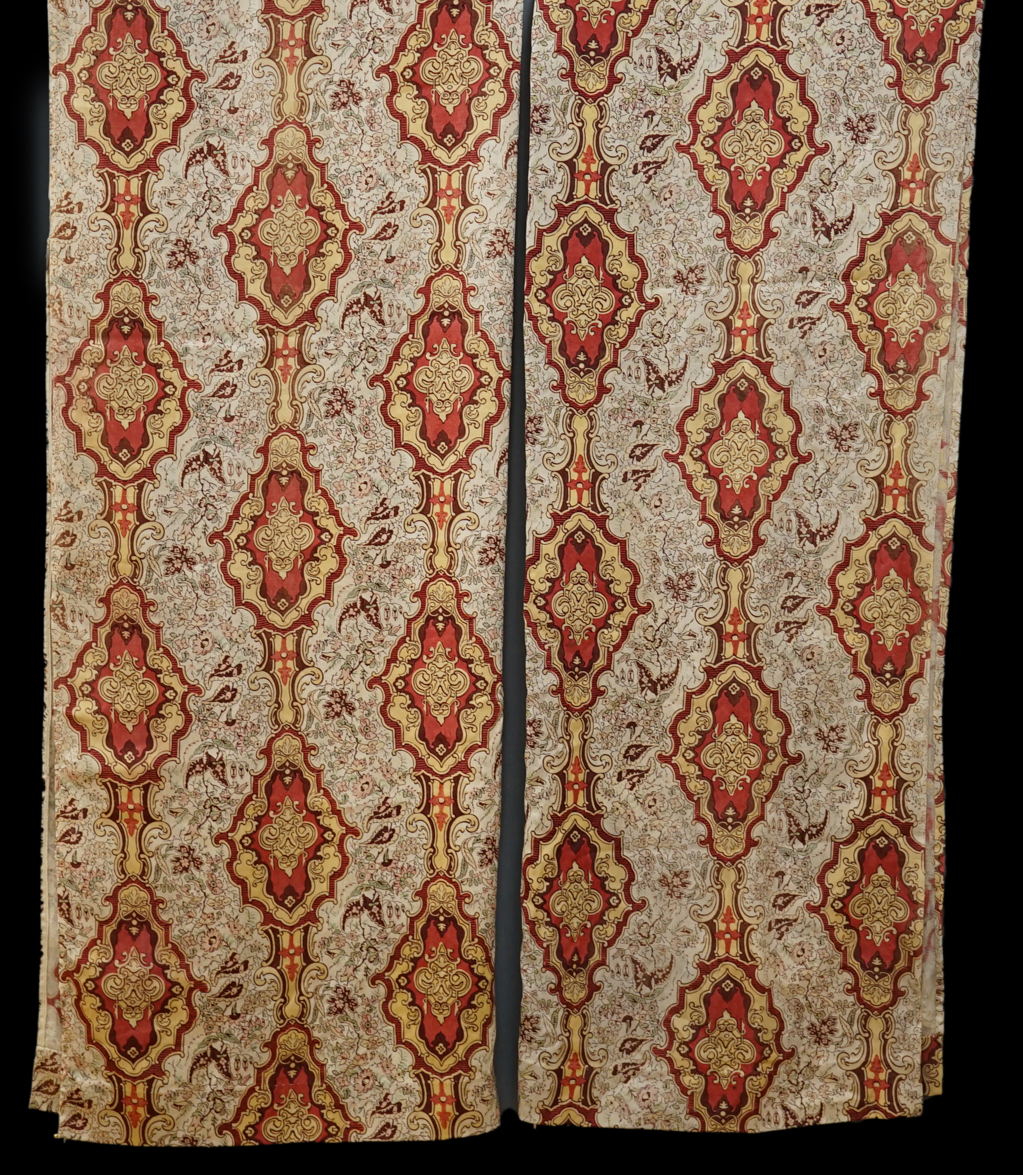 A pair of early 20th century block printed wool curtains, possibly French, made from two short looms (60cm each), printed in an ornate pattern in reds, ochres and greens, each curtain, 116cm wide x 208cm long. Condition